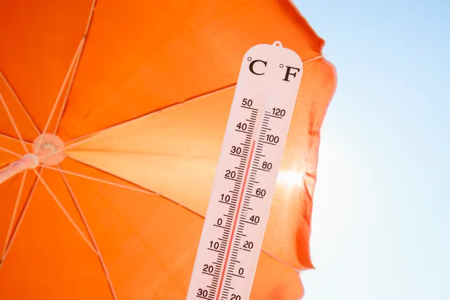 Termometru cu scală în grade Celsius și Fahrenheit, în fața unei umbrele portocalii, sub soare