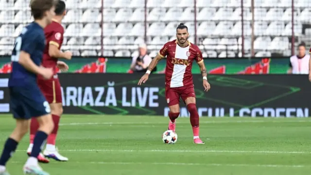 Fotbalist în echipament grena cu alb conducând mingea, urmărit de un adversar în albastru închis