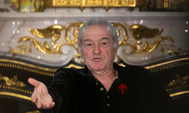 Bărbat cărunt, în bluză neagră cu o cruce roșie, întinzând mâna spre cameră într-un salon cu stucaturi aurite
