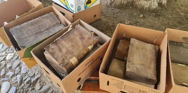 Cutii de carton pline cu cărți vechi legate în piele, așezate pe un pavaj de piatră