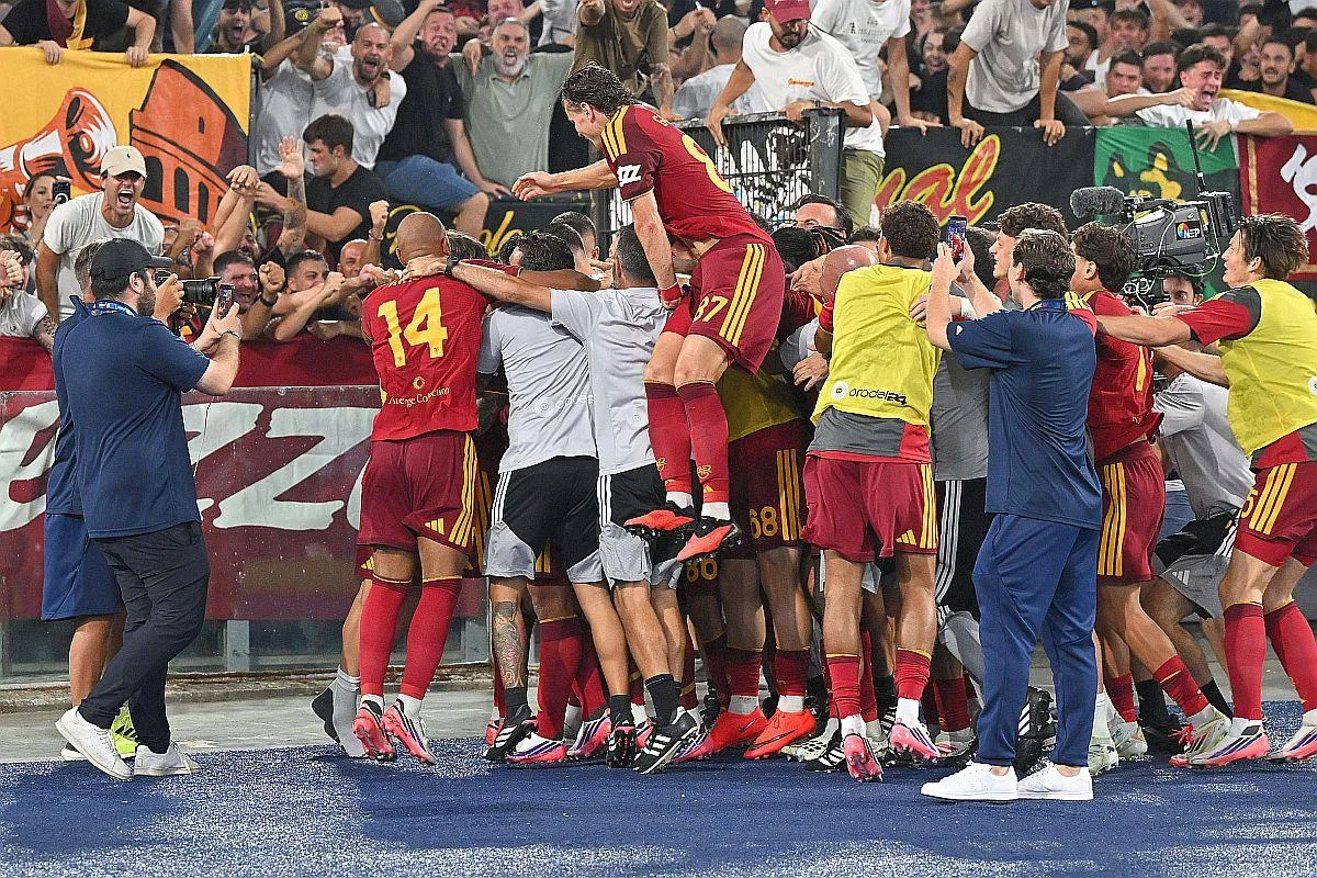 Fotbaliști în echipament vișiniu, îmbrățișându-se grămadă în fața suporterilor
