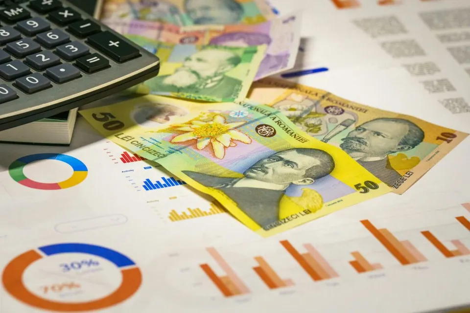 Bancnote românești, un calculator și grafice financiare tipărite, pe o masă