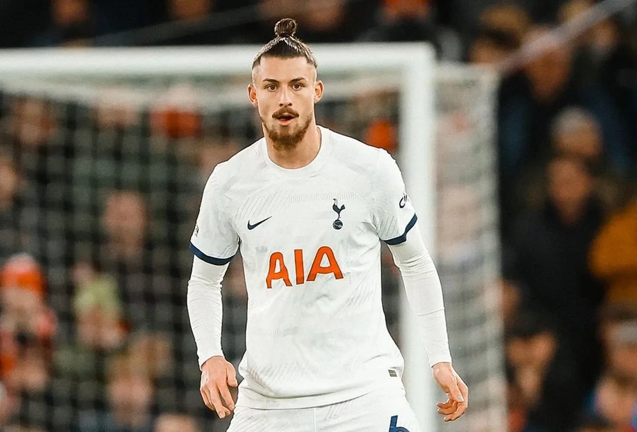 Fotbalist cu părul prins în coc, în tricoul alb Tottenham cu sponsorul AIA, pe teren