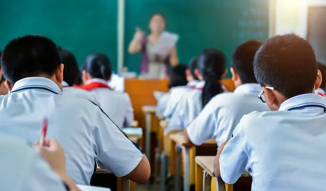 Elevi în uniforme albe, în bănci, cu profesoara la tablă, într-o sală de clasă