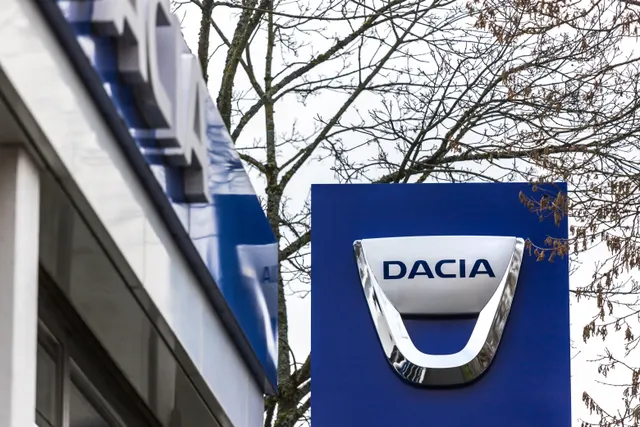 Sigla Dacia pe un panou albastru, în fața unei clădiri, lângă un copac desfrunzit