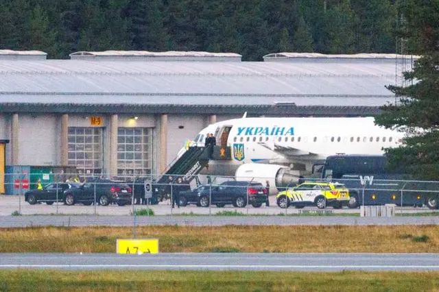 Avion cu inscripția „Україна” parcat pe aeroport, lângă o scară de îmbarcare și un șir de mașini