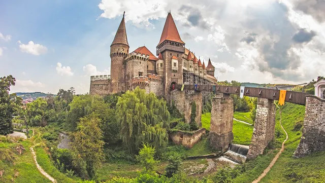 Castelul Corvinilor din Hunedoara, cu turnurile ascuțite și podul pe piloni, înconjurat de verdeață