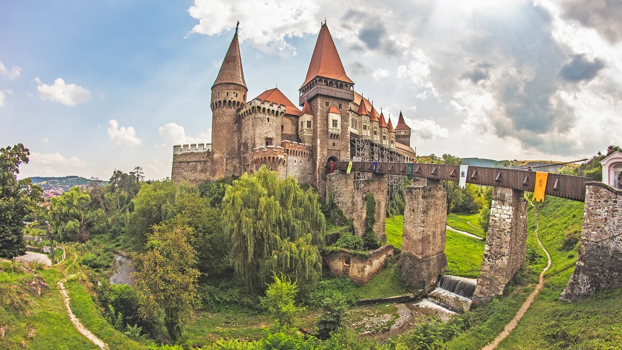 Castelul Corvinilor din Hunedoara, cu turnurile ascuțite și podul pe piloni, înconjurat de verdeață