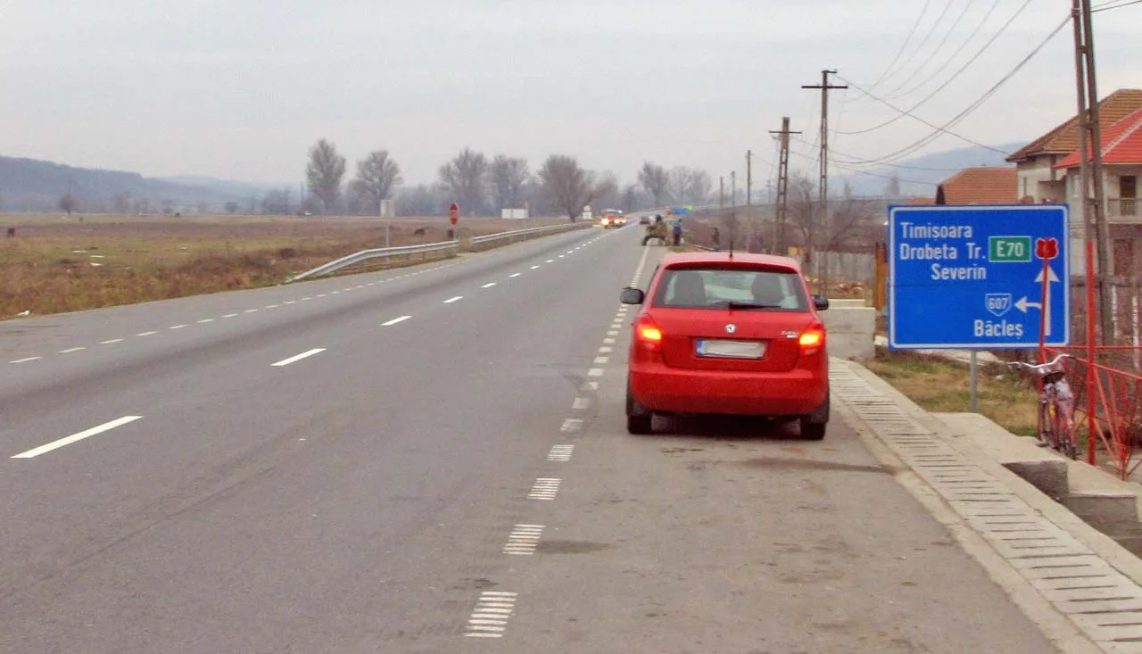 Drum național cu o mașină roșie și un indicator spre Timișoara și Drobeta-Turnu Severin