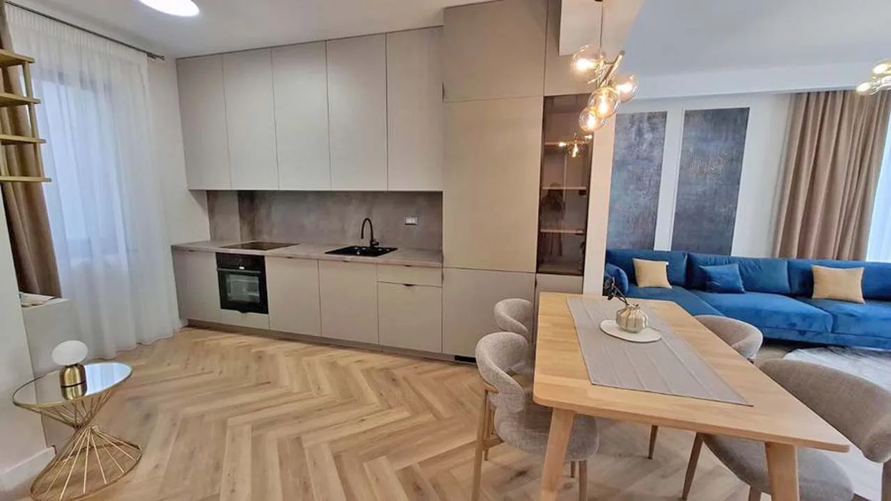 Apartament modern, cu bucătărie albă, parchet în spic, masă de lemn și o canapea albastră
