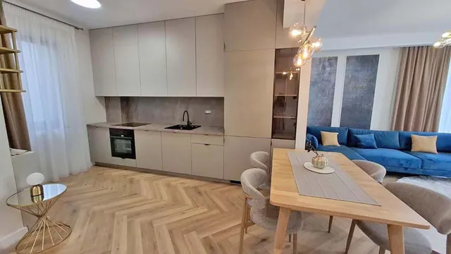 Apartament modern, cu bucătărie albă, parchet în spic, masă de lemn și o canapea albastră