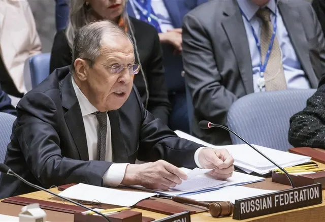 Bărbat cu ochelari, la masa cu plăcuța „Russian Federation”, citind documente, într-o ședință