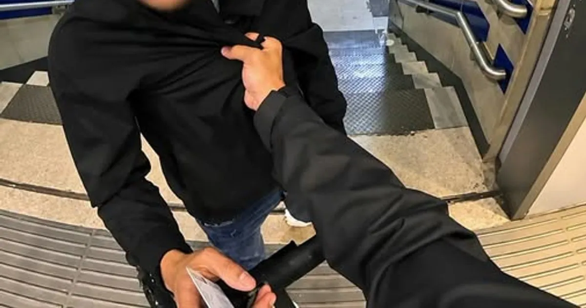 Mână care apucă de geacă un bărbat îmbrăcat în negru, pe niște scări cu balustradă metalică