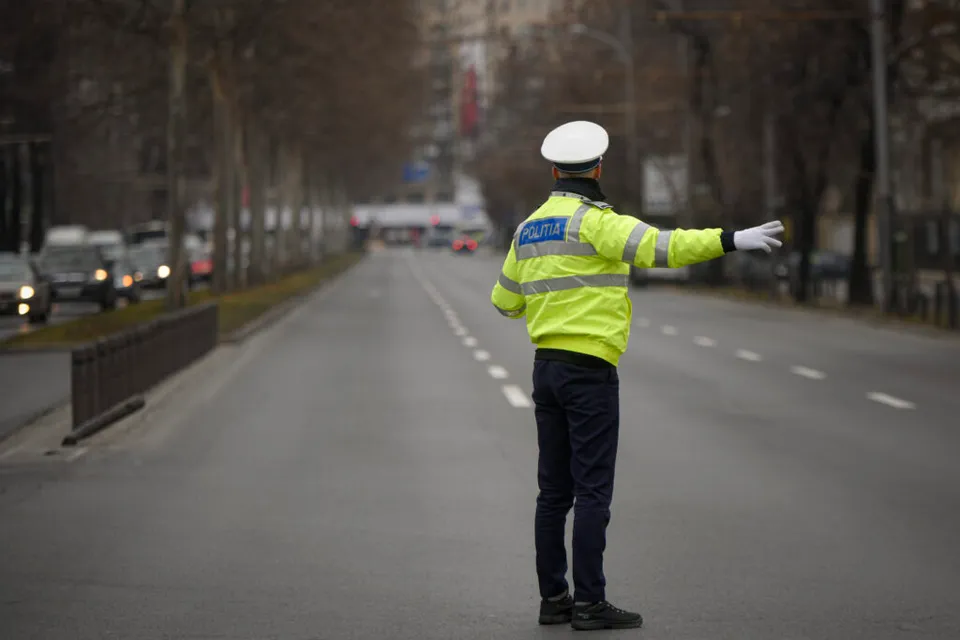Polițist rutier cu chipiu alb și vestă reflectorizantă, dirijând circulația pe un bulevard gol
