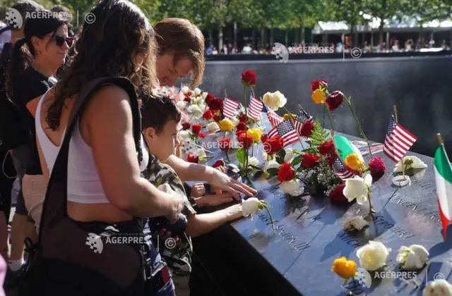 Oameni care așază flori și steaguri americane pe parapetul de bronz al memorialului 11 Septembrie
