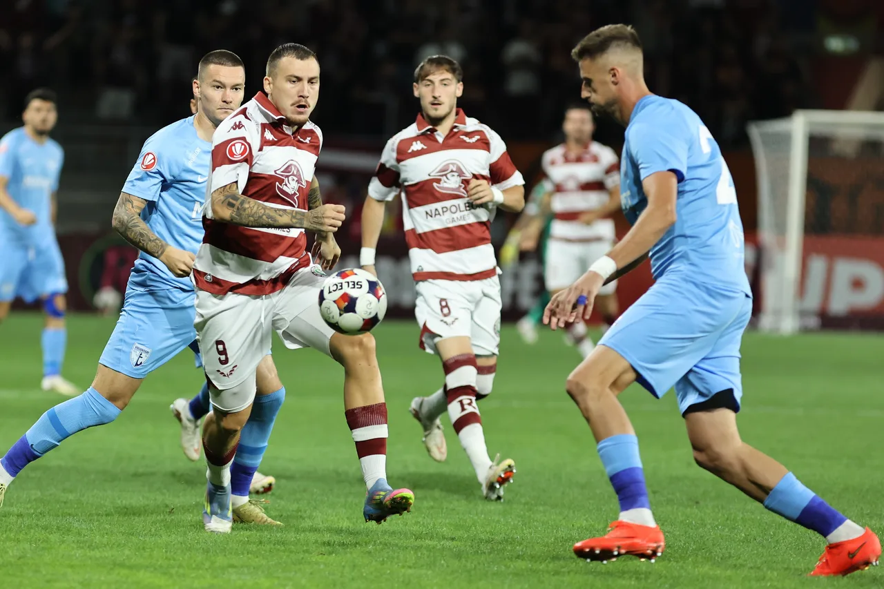 Fotbaliști în alb cu dungi vișinii și în albastru deschis, în duel pentru minge, la meciul Rapid-Voluntari
