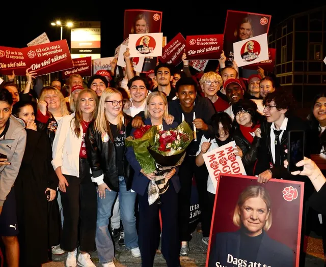 Susținători cu pancarte roșii și flori la un miting nocturn, în jurul unei femei blonde