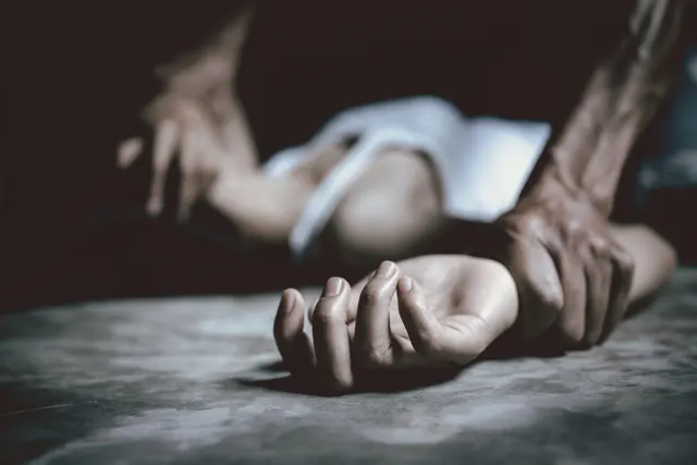 Mână care apucă brațul unei persoane întinse pe podea, într-o lumină întunecată