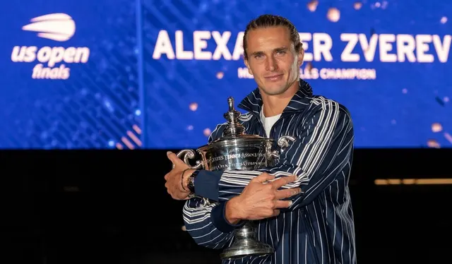 Alexander Zverev cu trofeul US Open în brațe, în fața ecranului cu numele său