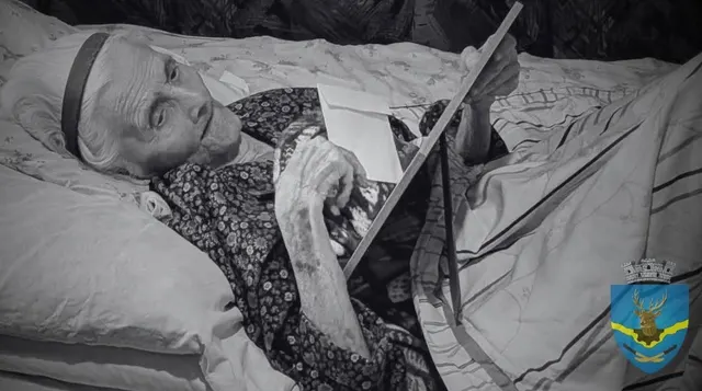 Noja Paladia, în pat, ținând o diplomă înrămată, într-o fotografie alb-negru