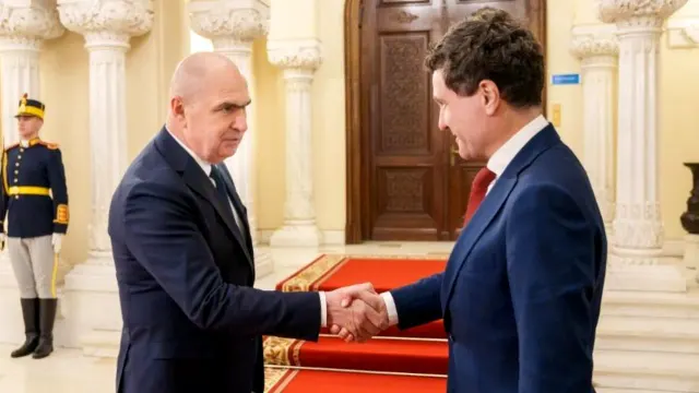 Doi bărbați dându-și mâna într-un salon cu coloane albe, lângă un militar din garda de onoare