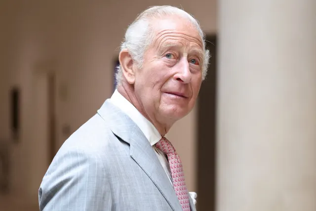 Regele Charles al III-lea, în costum gri deschis și cravată roz, în timpul unei vizite în Oxfordshire