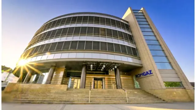 Sediul Romgaz, o clădire cu fațadă curbată din sticlă și sigla companiei, în lumina soarelui