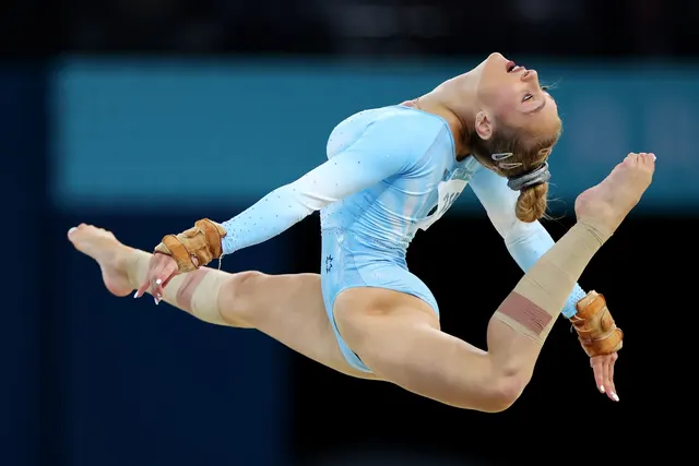 Gimnastă în costum albastru deschis, într-un salt cu picioarele întinse în sfoară