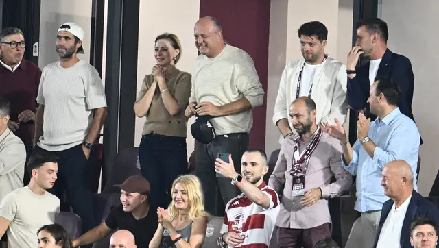 Spectatori într-o lojă de stadion, aplaudând, unii în picioare, alții așezați