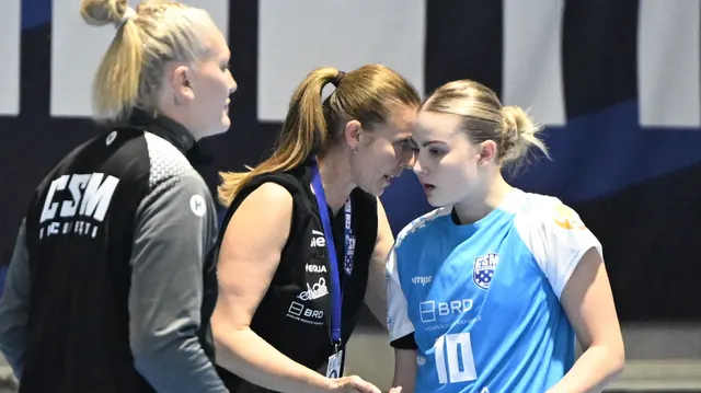 Trei sportive discută într-o sală de sport; una are o geacă neagră cu inscripția „CSM”, alta tricoul albastru nr. 10