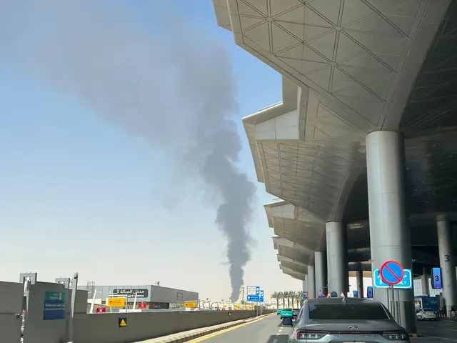 Coloană de fum negru care se ridică în depărtare, văzută de lângă o clădire modernă cu copertină
