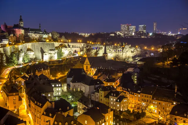 Vedere de noapte asupra orașului Luxemburg, cu cartierul vechi luminat și clădiri înalte în fundal
