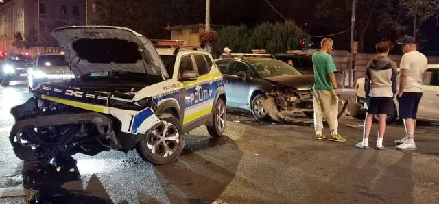 Mașină de poliție cu partea din față distrusă după o coliziune, noaptea, cu oameni pe trotuar