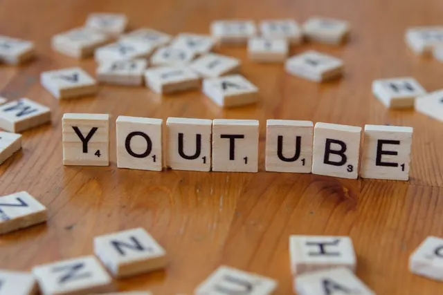 Piese de joc cu litere care formează cuvântul „YOUTUBE”, pe o masă de lemn