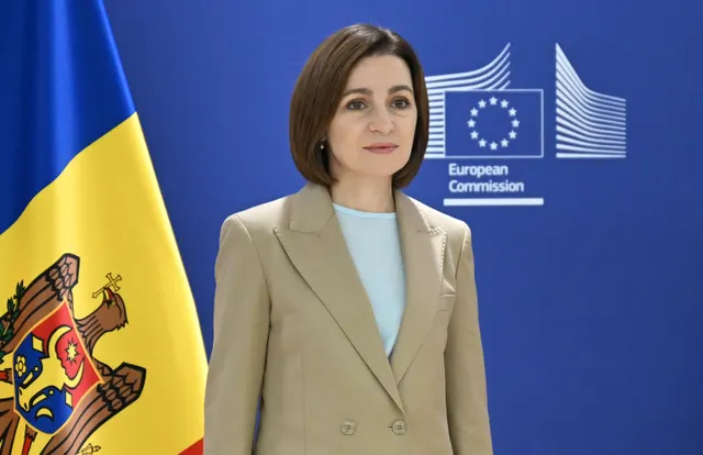 Femeie în sacou bej, în fața drapelului Republicii Moldova și a siglei Comisiei Europene