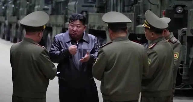 Kim Jong Un, în geacă închisă, discutând cu ofițeri în uniforme, lângă vehicule militare