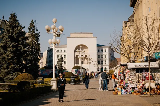 Clădirea Operei din Timișoara, văzută de pe o alee pietonală cu felinare și tarabe