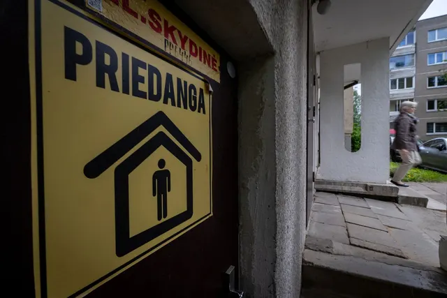 Panou galben cu inscripția „PRIEDANGA” și simbolul de adăpost, la intrarea unui bloc