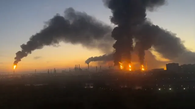 Coloane de fum negru și flăcări deasupra unei zone industriale, la apus