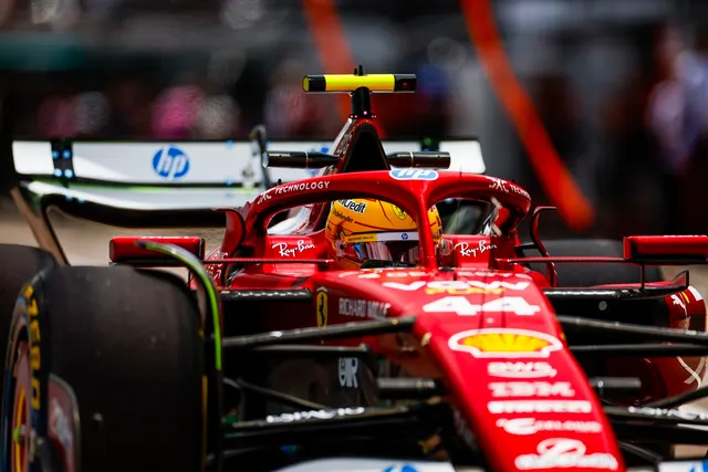 Monopost Ferrari roșu de Formula 1, cu pilotul în cockpit, în fața unui panou HP