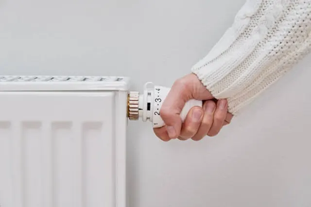 Mână care reglează robinetul termostatic al unui calorifer alb