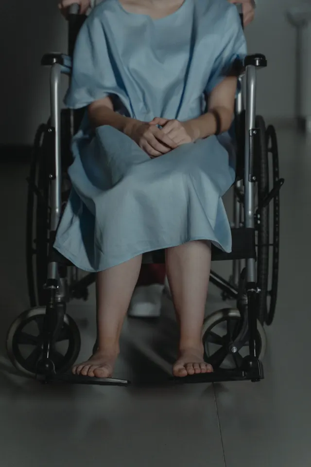 Pacient în halat de spital stând într-un scaun cu rotile, cu fața în afara cadrului