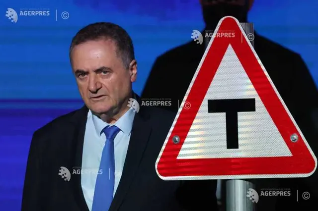 Bărbat în costum și cravată albastră, lângă un indicator rutier triunghiular cu litera T