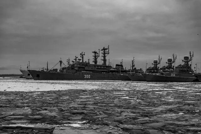 Nave de război ancorate într-un port, cu sloiuri de gheață pe apă, în alb-negru