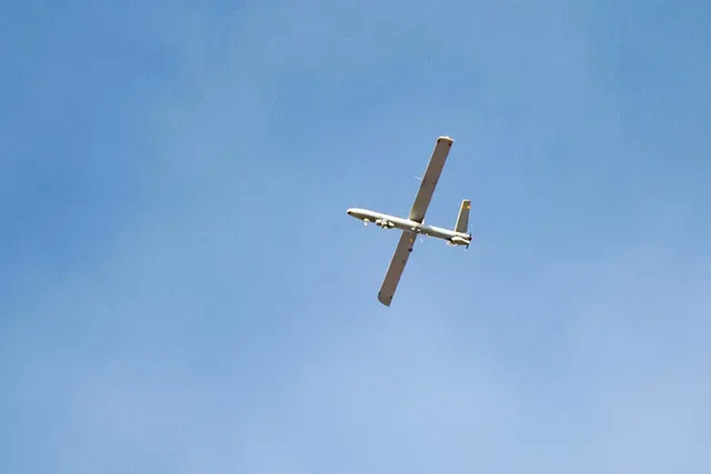 Dronă militară în zbor pe cerul senin, văzută de jos
