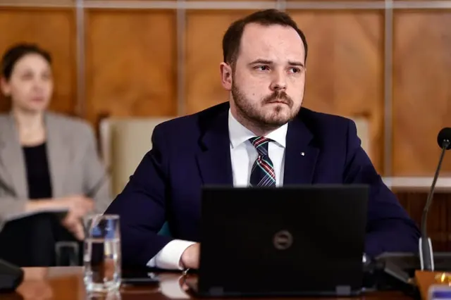 Alexandru Rogobete, cu barbă, în costum, la o masă cu laptop, într-o sală de ședințe