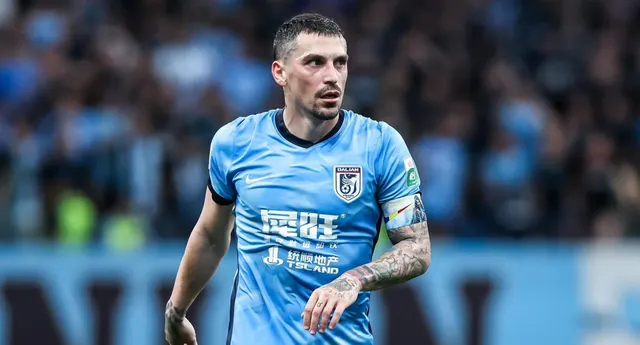 Fotbalist în tricou bleu cu inscripții în chineză, cu brațul tatuat, pe un stadion