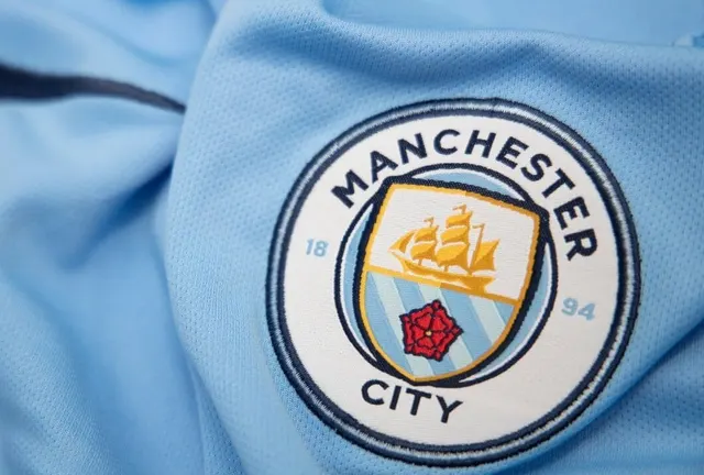Emblema Manchester City brodată pe un tricou bleu, în prim-plan
