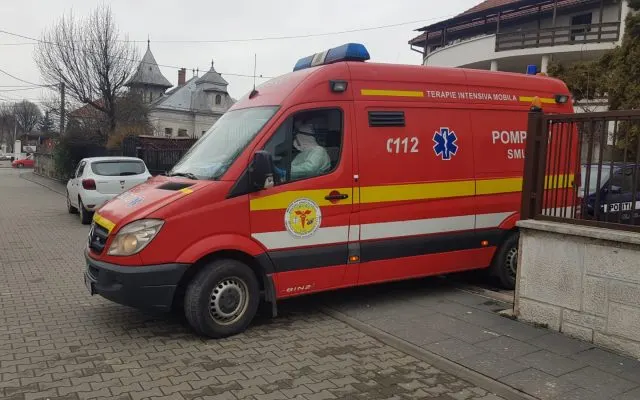 Ambulanță SMURD roșie, cu inscripția 112, parcată pe o stradă cu case