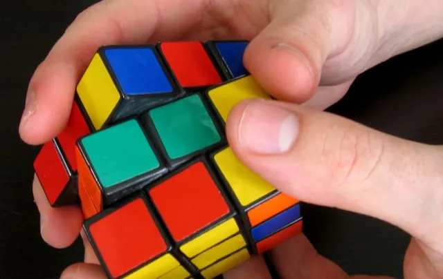 Mâini care rotesc un cub Rubik cu fețe colorate, în prim-plan
